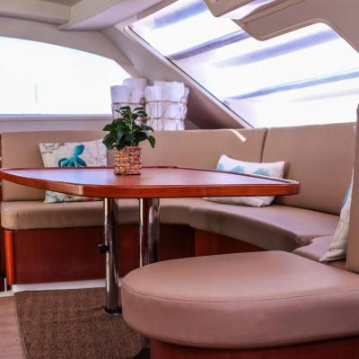 Boat interior with wooden table, beige seating, pillows, and a plant.