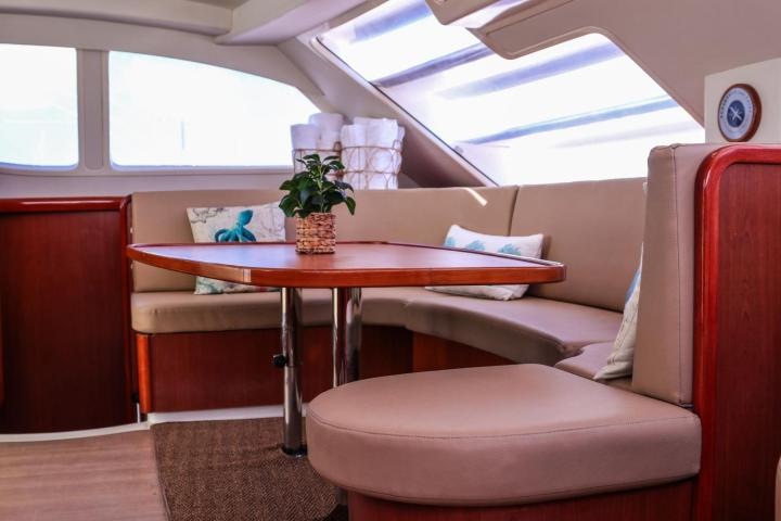 Boat interior with wooden table, beige seating, pillows, and a plant.