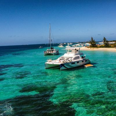 Catamarans anchored near a sandy beach with clear turquoise water and blue sky.