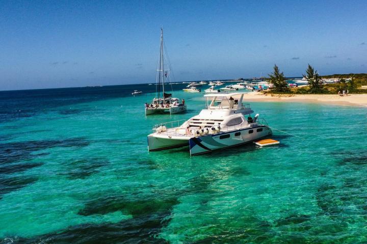 Catamarans anchored near a sandy beach with clear turquoise water and blue sky.
