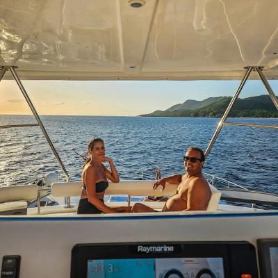 Two people seated on a boat at sea with mountains in the background during sunset.