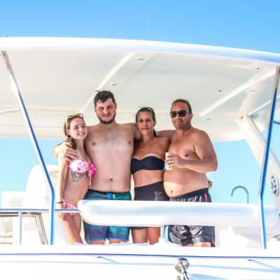 Four people in swimwear standing on a boat under a canopy.