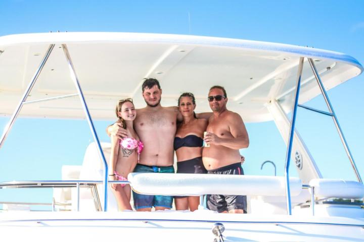Four people in swimwear standing on a boat under a canopy.