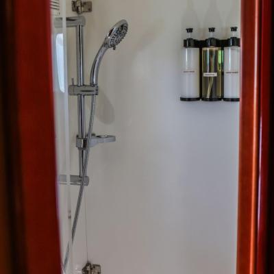 Small shower with metal showerhead and soap dispensers on white wall.